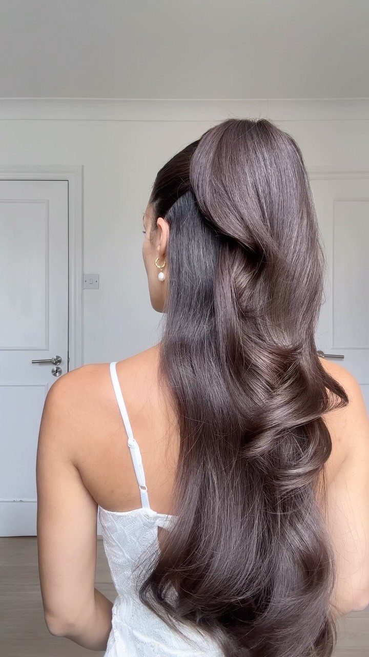 11 Half Up Half Down Wedding Hair Styles You'll Love 8 Voluminous brown half-ponytail with cascading curls on a woman in a white top.