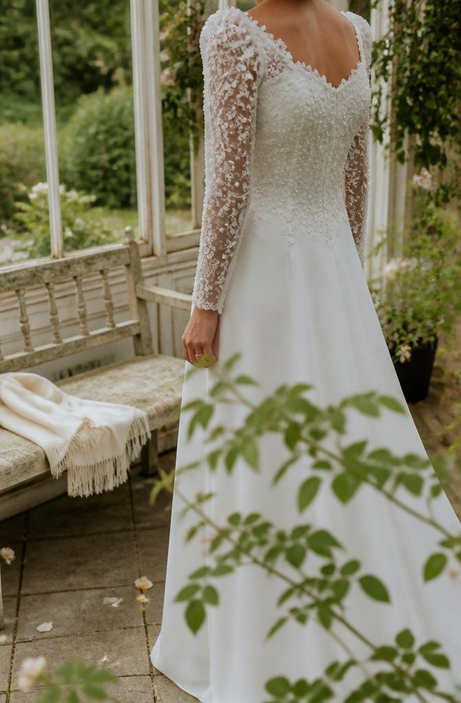 Bride near a garden in a gown with floral lace appliqués on the bodice and sleeves