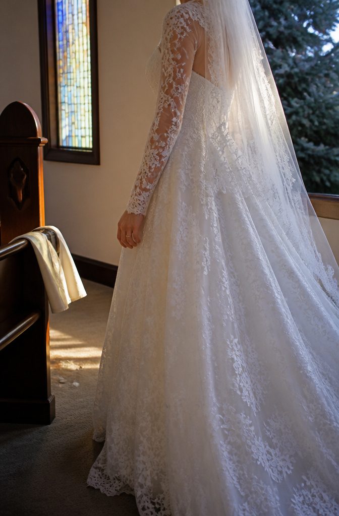 Bride at a fitting in sheer floral lace sleeves and a long veil