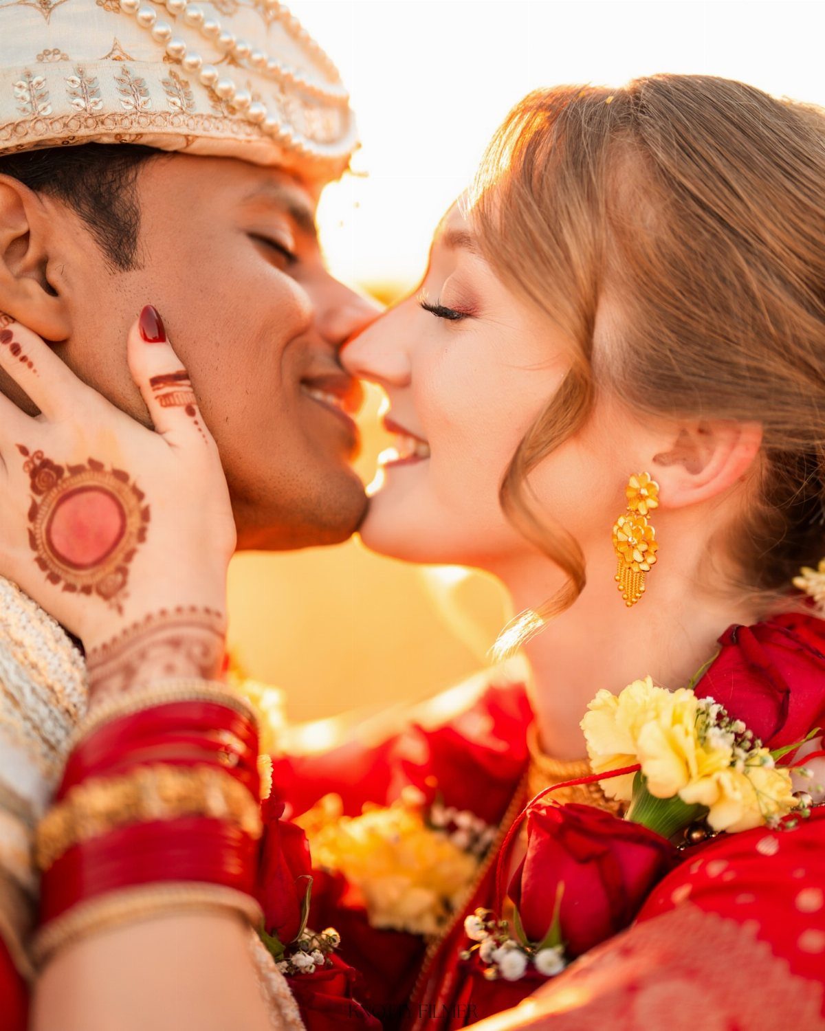 Bride and groom in traditional Indian wedding attire leaning in for a kiss.