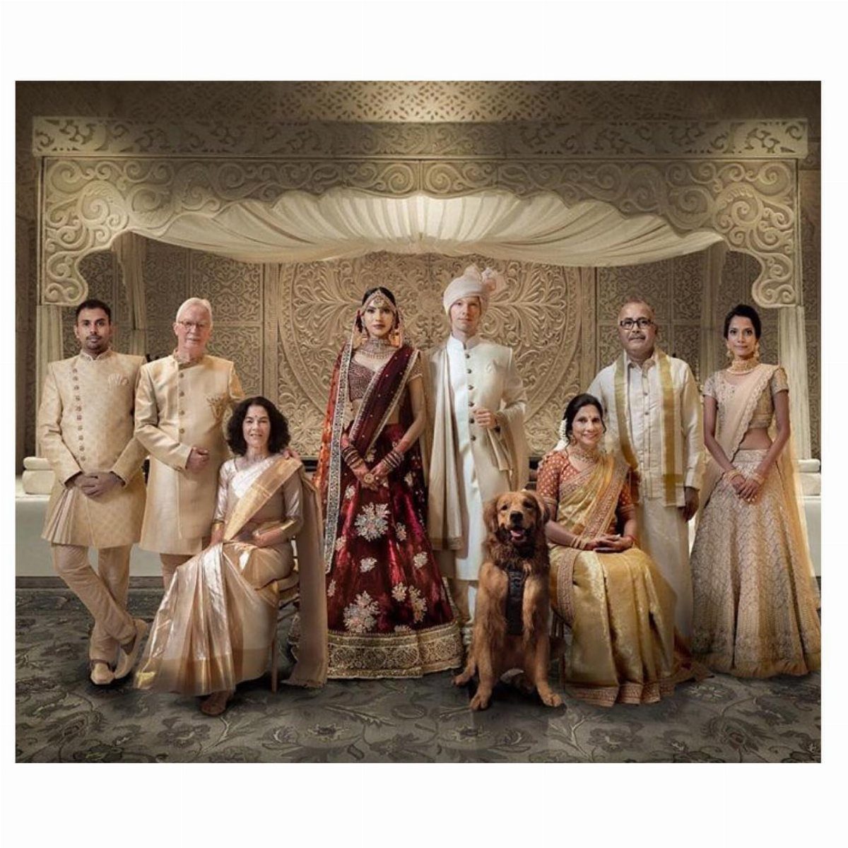 Indian wedding couple posing with parents and a golden retriever in ornate room