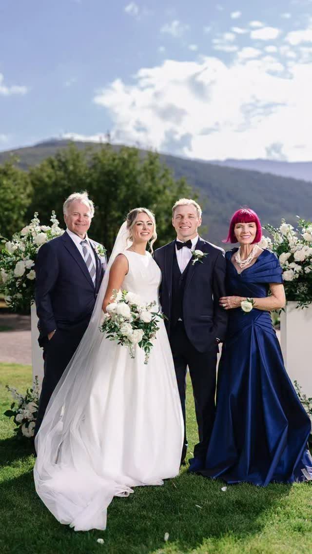 Bride and groom posing with a middle-aged couple on a grassy outdoor wedding venue.