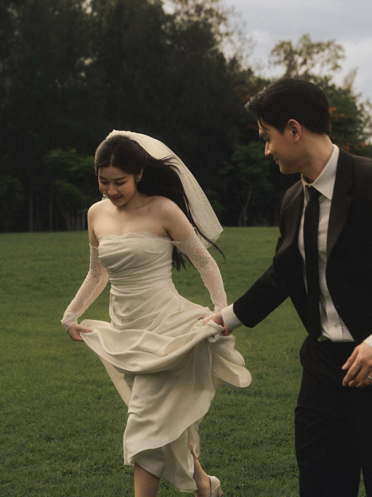 Bride and groom in a grassy field with the groom lifting her dress.