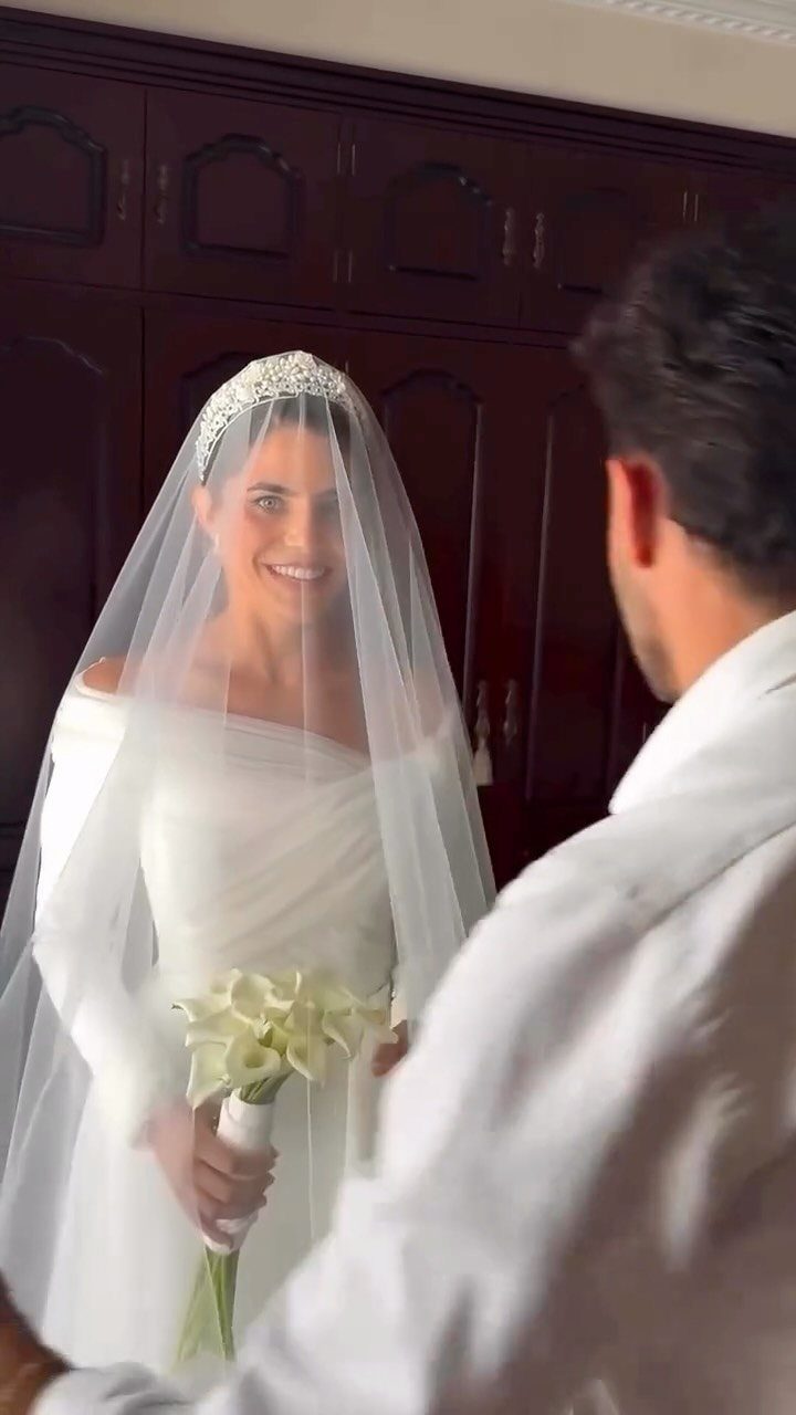 Bride in white gown and veil smiling at groom during a first look.