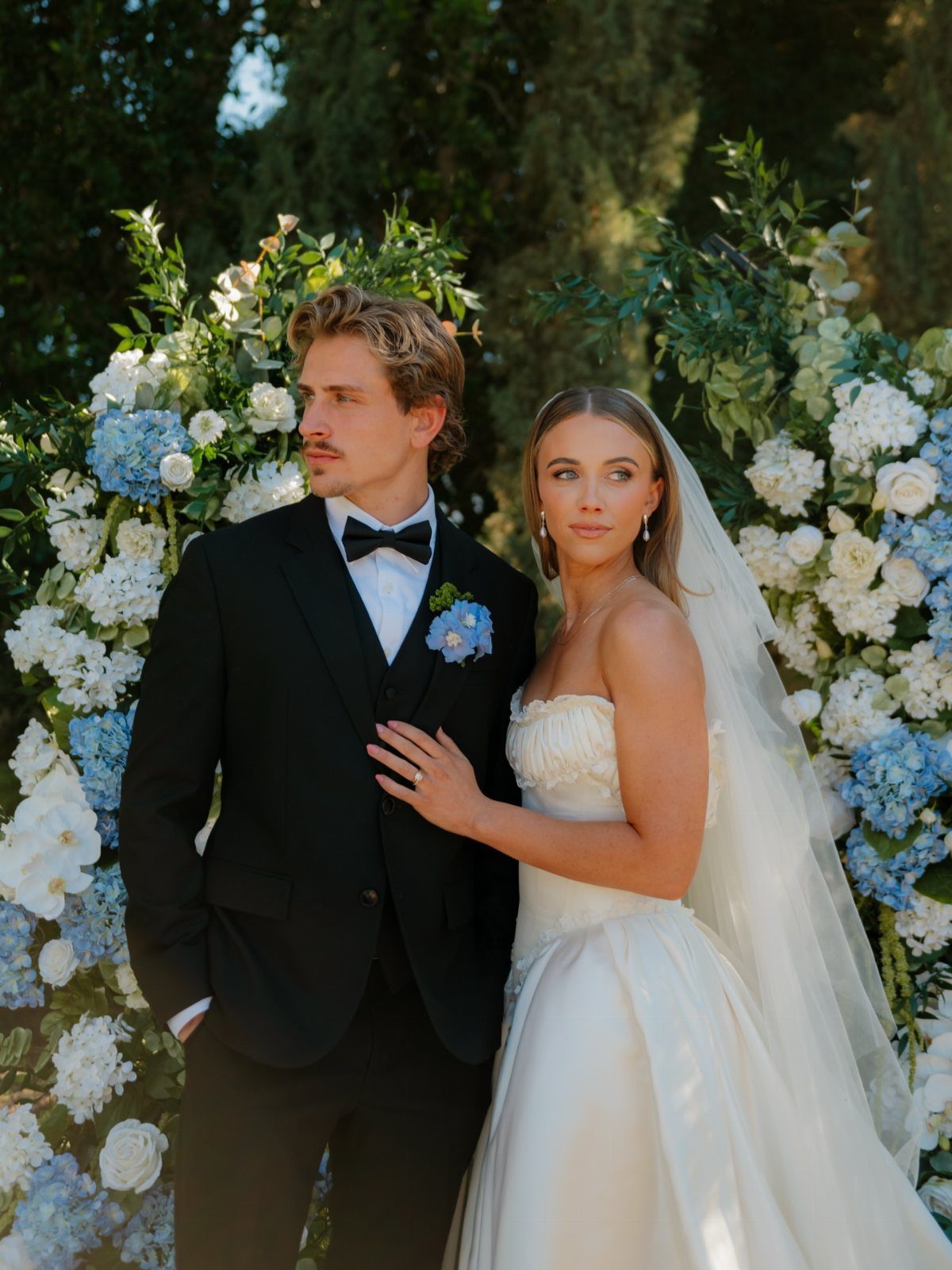 Bride and groom posing together in front of a white and blue floral wall.
