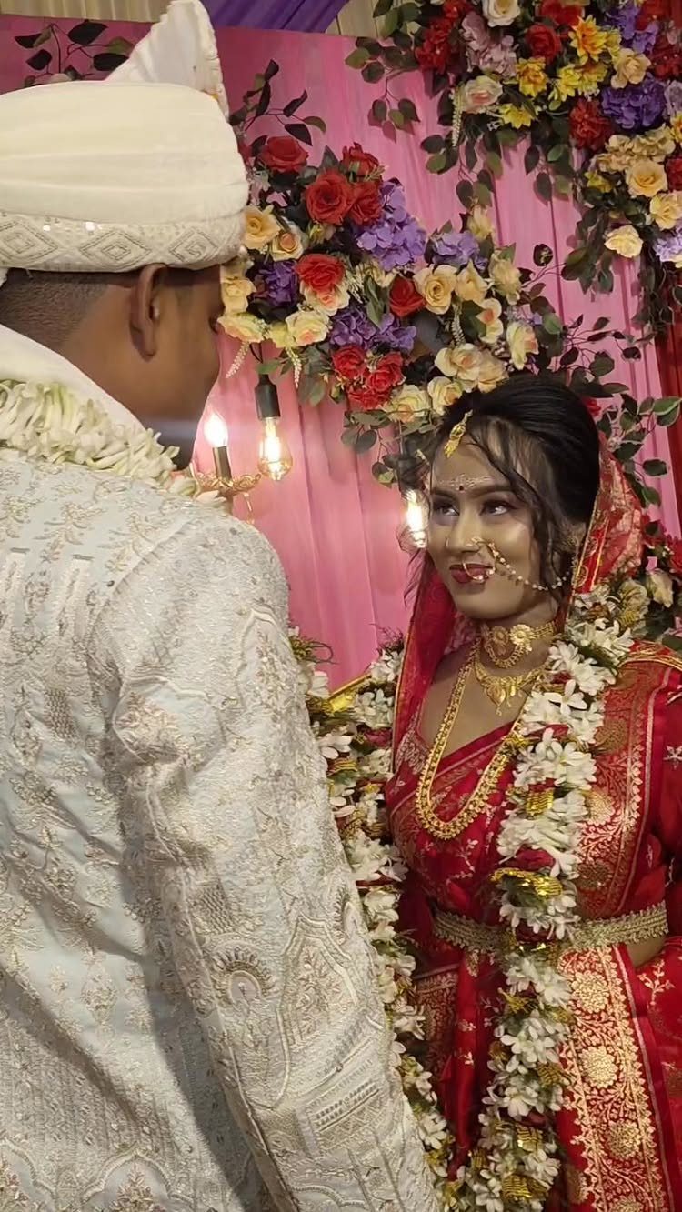 Bride in red sari and groom in white sherwani facing each other with garlands.