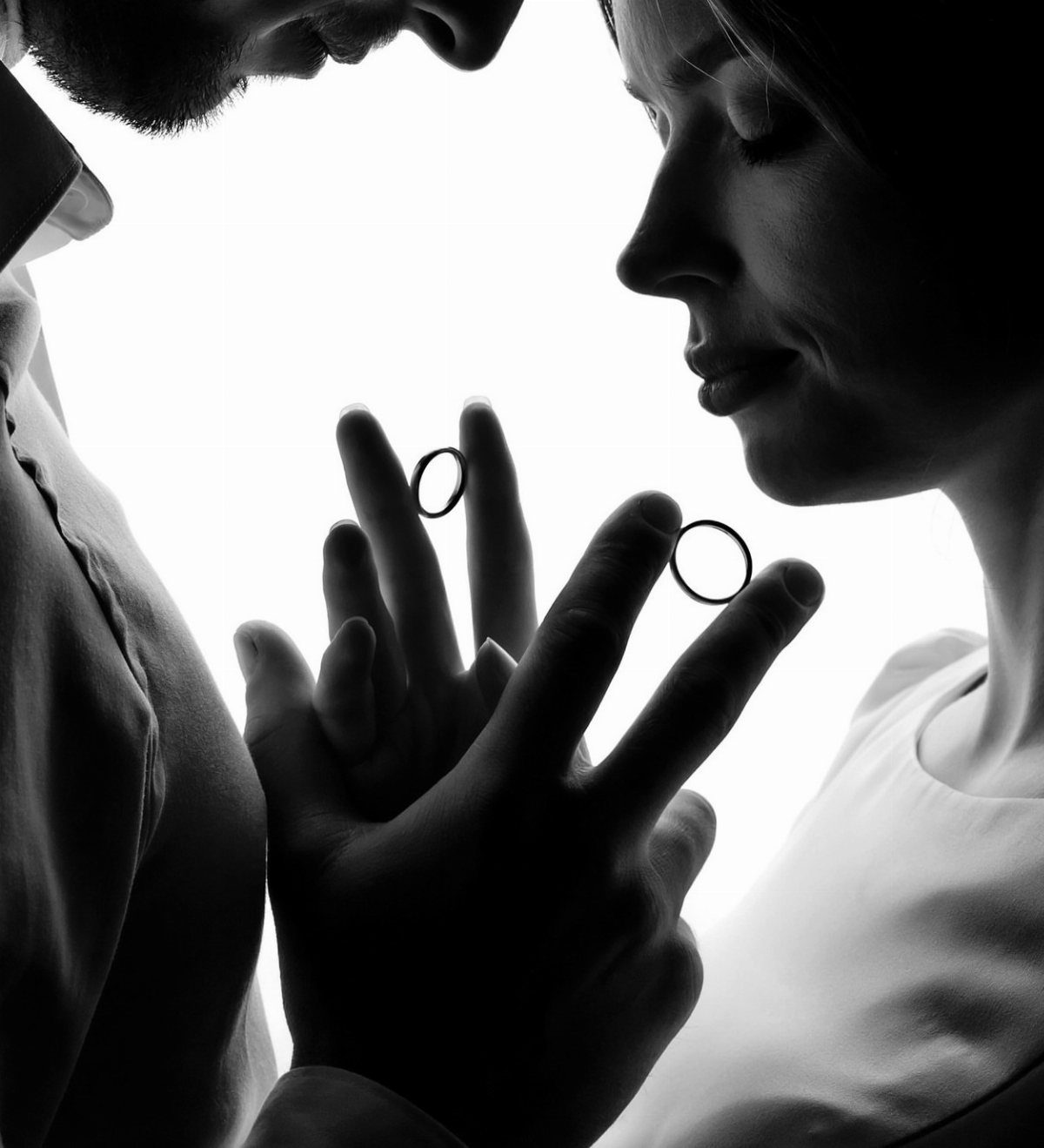Silhouette of a couple facing each other with wedding rings visible on their fingers.