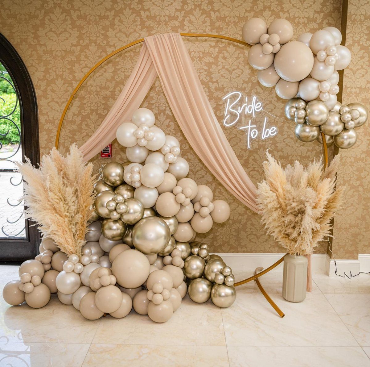 Gold circular backdrop with cream and gold balloon garlands and pampas grass.