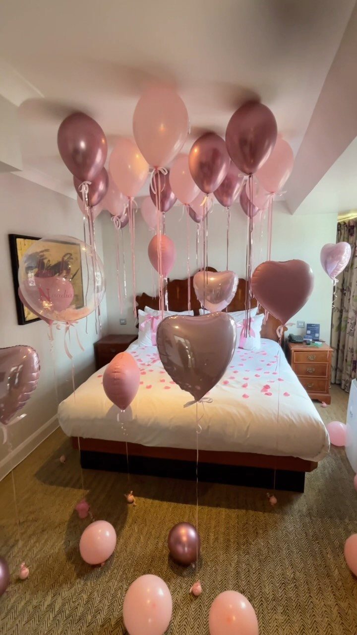 Pink and rose gold balloons floating over a white bed in a bedroom.