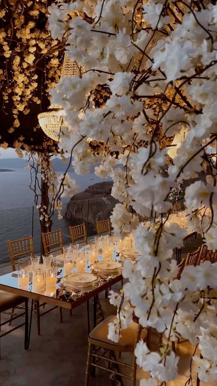Elegant outdoor dining table with white floral canopy and glowing candles by the sea