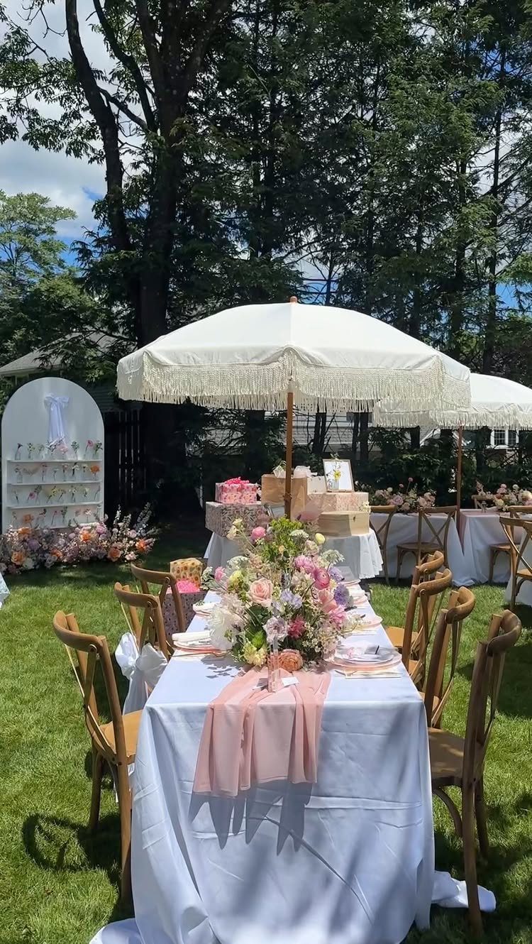 Floral centerpiece with pink and white flowers on a white table under umbrellas.