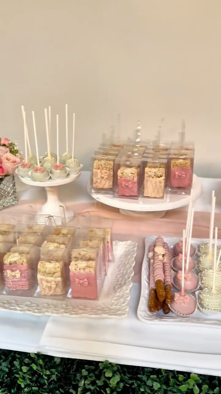 Dessert table with cake pops and treats in clear boxes with pink ribbons.