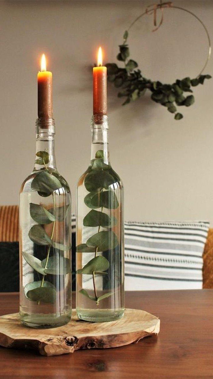 14 Candle Table Decor Ideas for Centerpieces That Feel Considered 8 Two wine bottles with eucalyptus stems and lit taper candles on a wooden base.