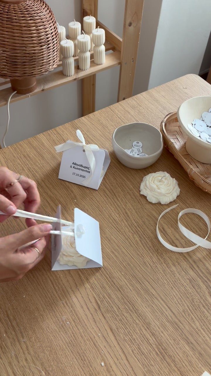 9 Candle Wedding Favors: From Beach Gel to Flower-Topped Votives 2 Hands assembling small white paper gift boxes on a wooden table with ribbons and candles nearby.
