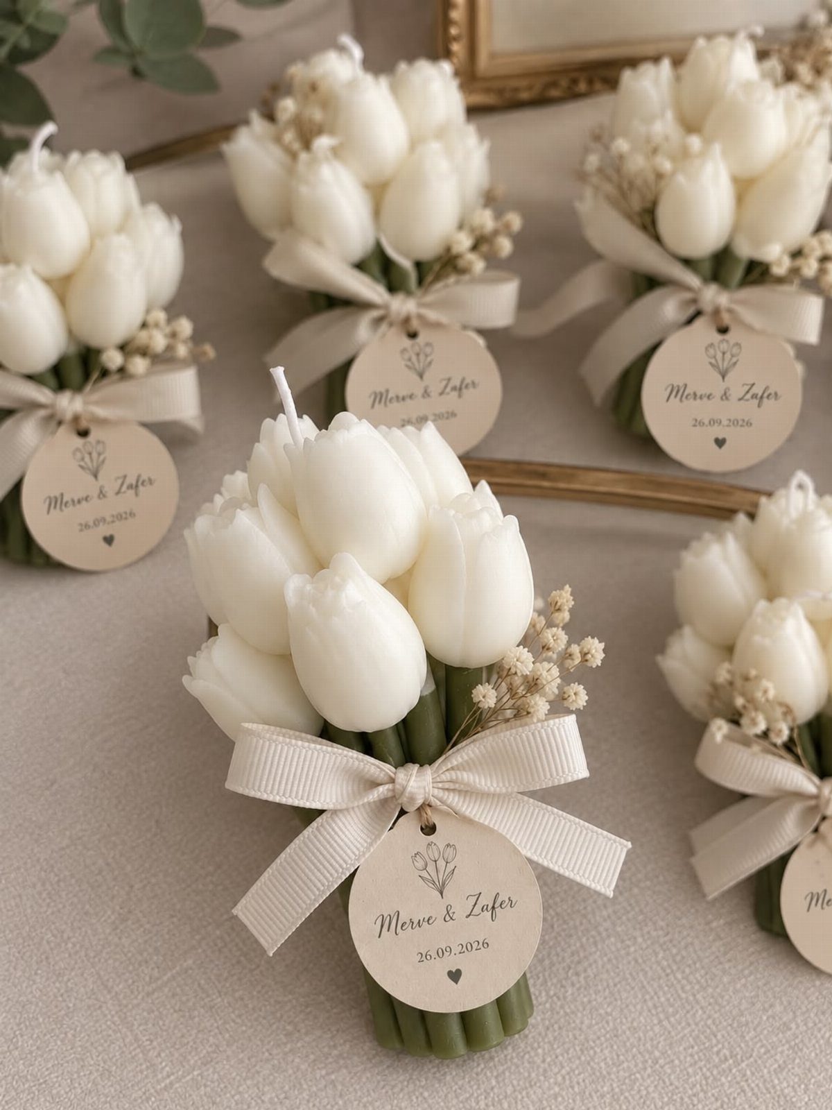 9 Candle Wedding Favors: From Beach Gel to Flower-Topped Votives 5 White tulip-shaped candles tied with cream ribbons and personalized paper tags on a neutral background.