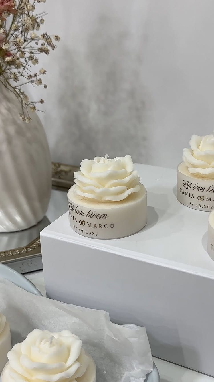 9 Candle Wedding Favors: From Beach Gel to Flower-Topped Votives 3 White rose-shaped candles with personalized text sitting on a white display stand.