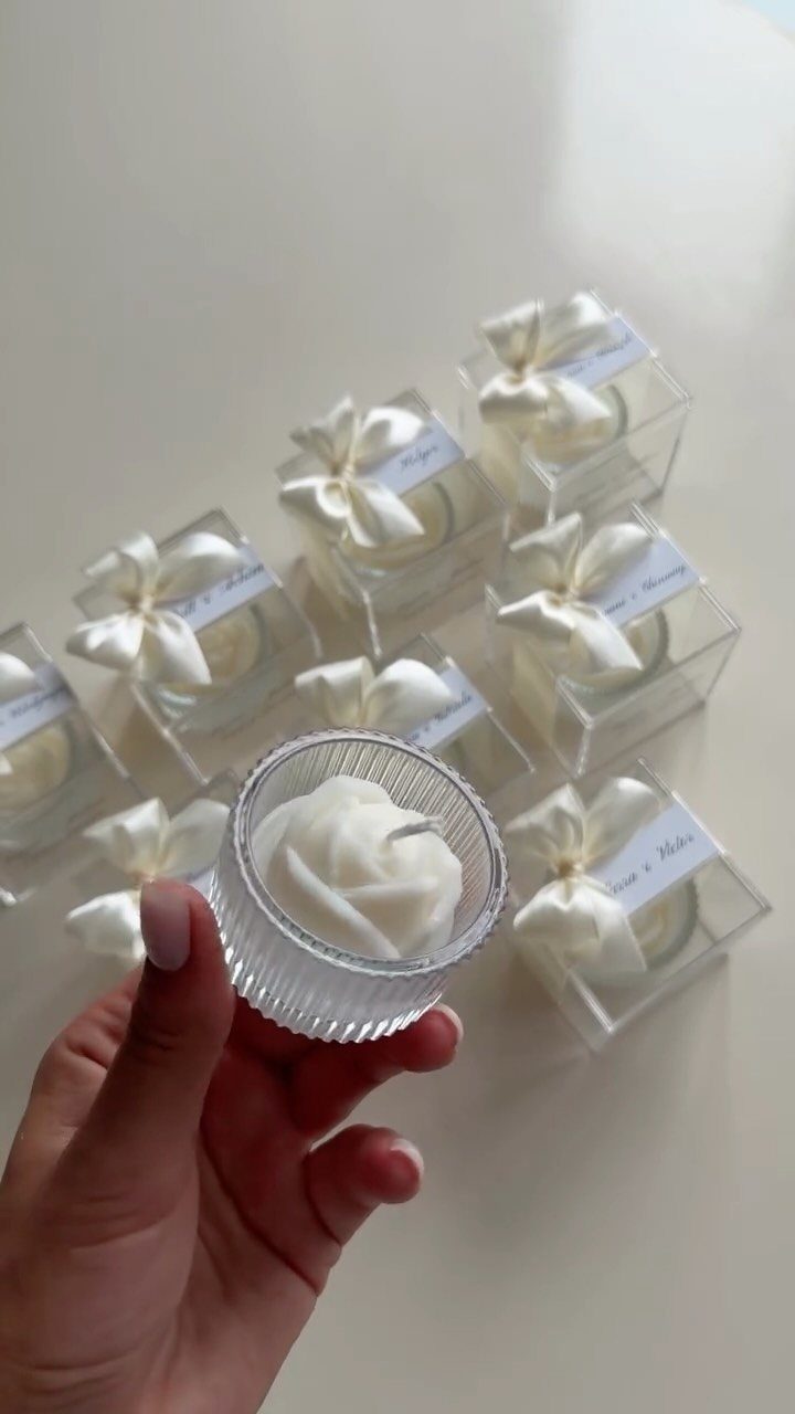9 Candle Wedding Favors: From Beach Gel to Flower-Topped Votives 7 A hand holding a small ribbed glass candle with white wax against a background of packaged candles.