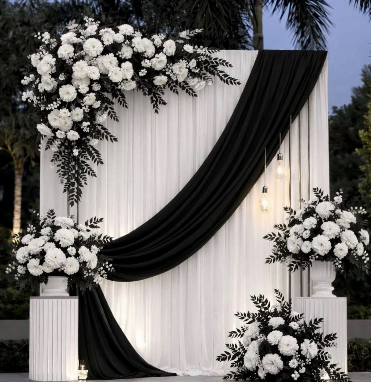 21 Color Combinations for Wedding Palettes in 2026 12 White wedding backdrop with black fabric draping and white floral arrangements on pedestals.
