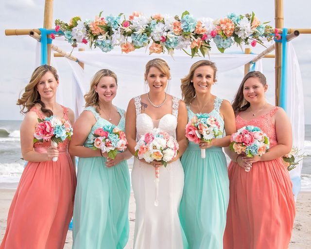 21 Color Combinations for Wedding Palettes in 2026 3 Bridesmaids in coral and mint dresses standing with a bride on a beach.
