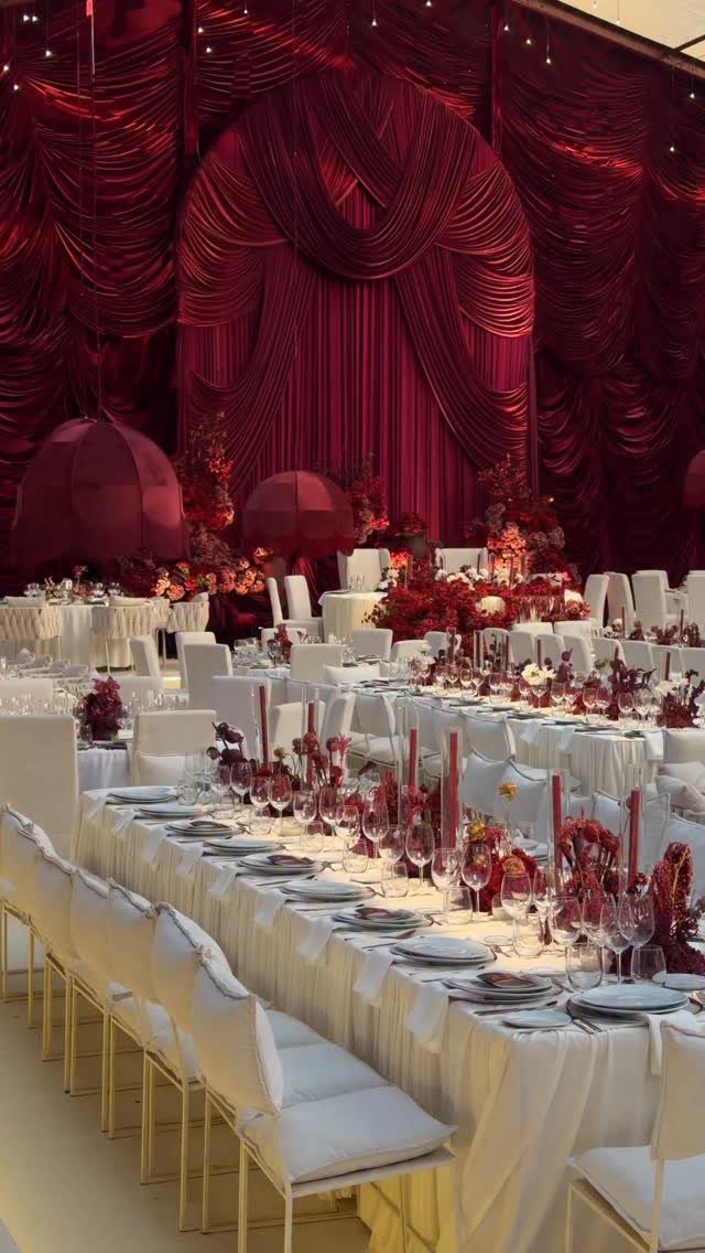 21 Color Combinations for Wedding Palettes in 2026 19 Long banquet tables with white linens and red floral arrangements set against red draped fabric.