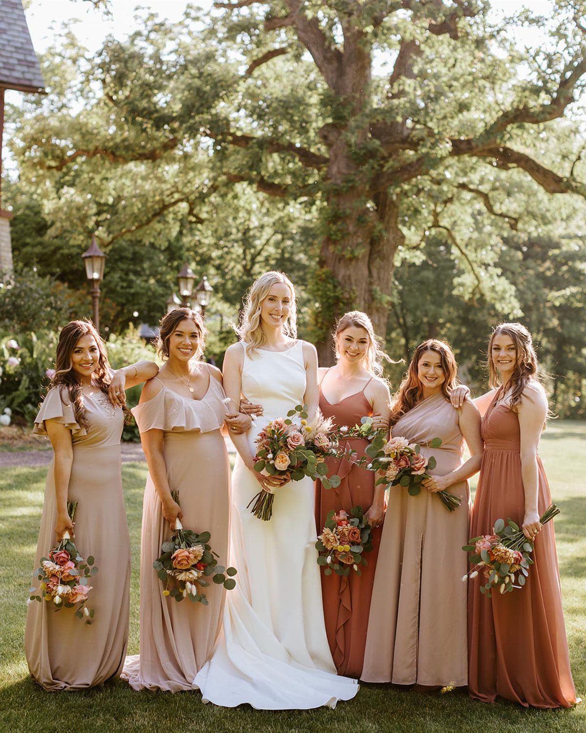21 Color Combinations for Wedding Palettes in 2026 20 A bride and her bridesmaids posing in a garden wearing coordinated wedding color palette dresses.
