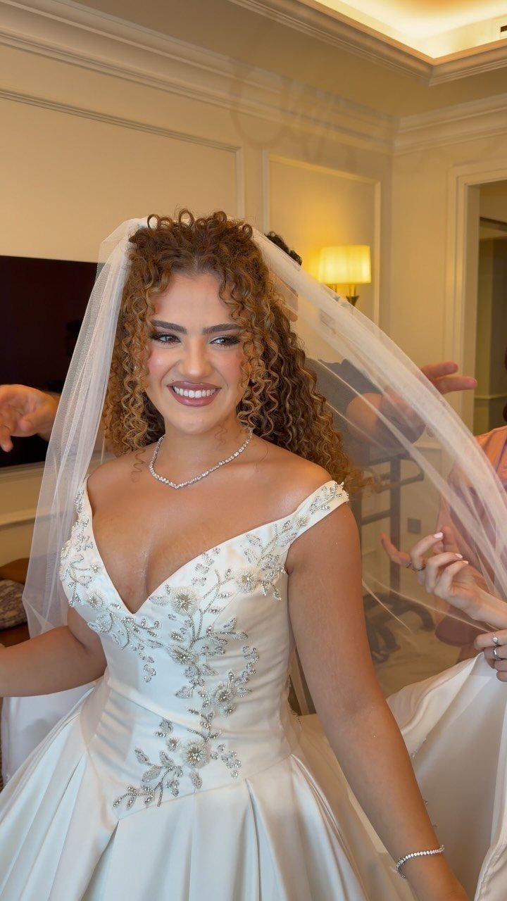 Bride with long golden-brown curly hair wearing a white embroidered wedding dress and veil.