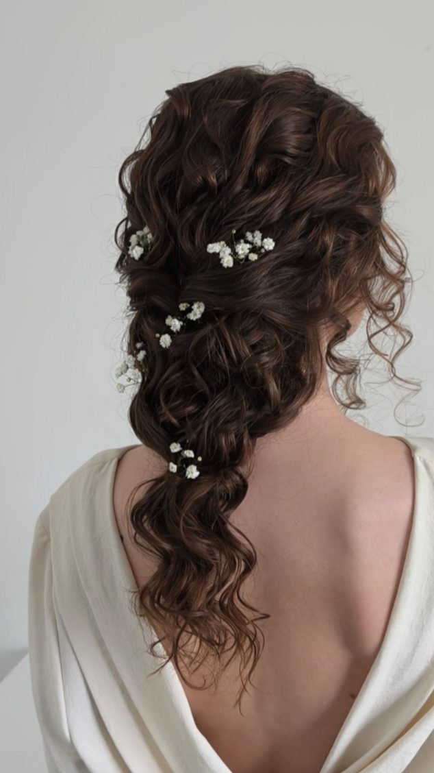 Curly brown hair styled in a romantic wedding updo with small white flowers.