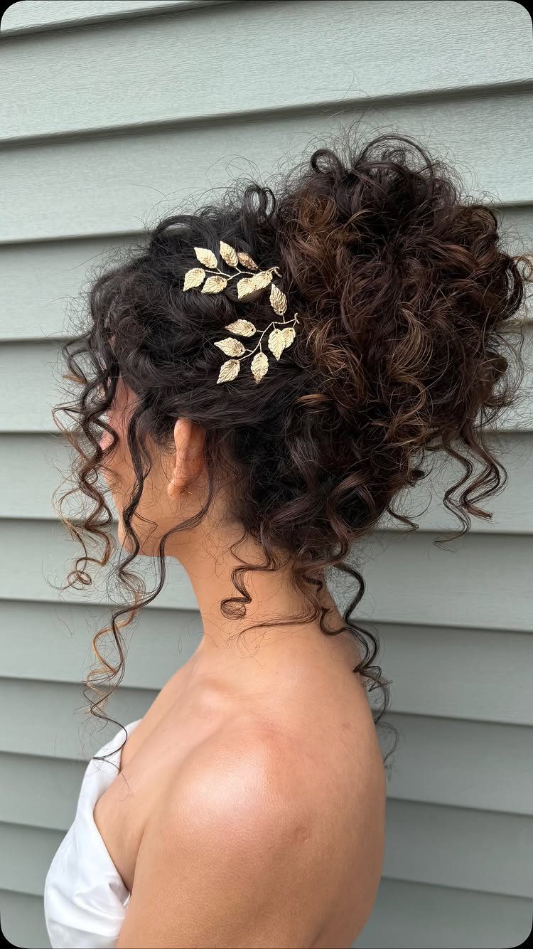 Woman with curly hair in a wedding updo featuring a gold leaf accessory.