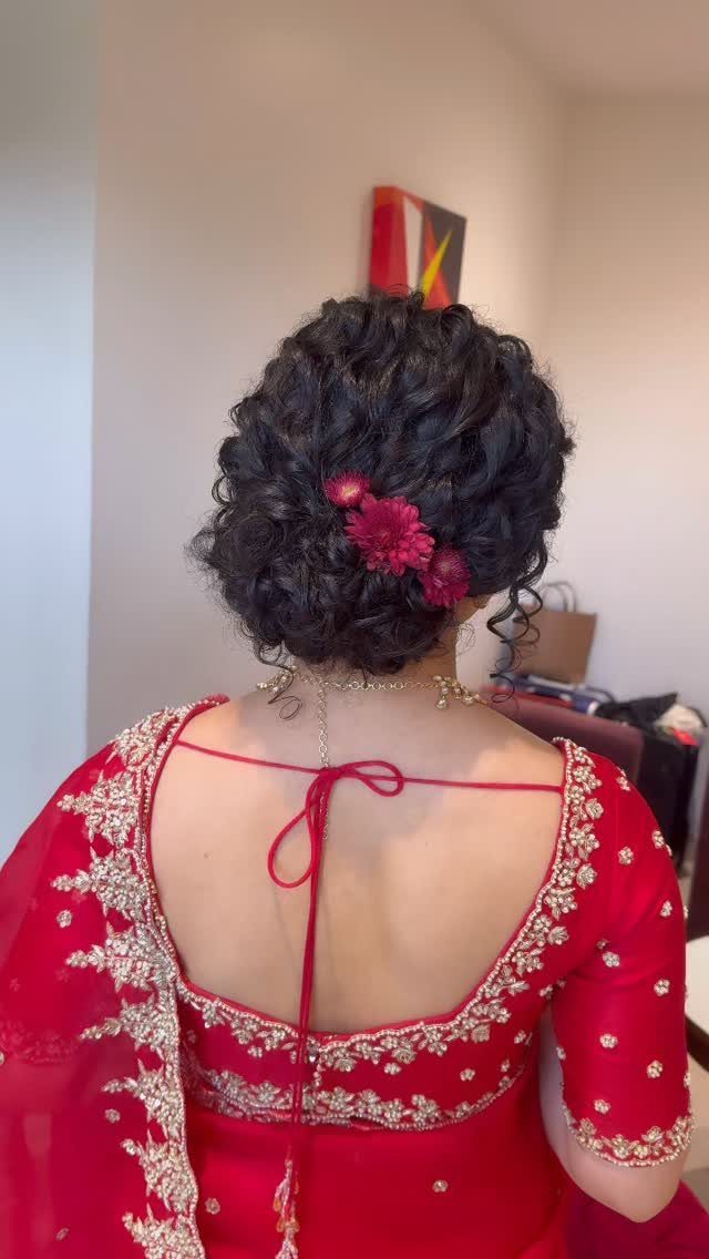 Dark curly hair styled in an updo with red flowers and red bridal attire.