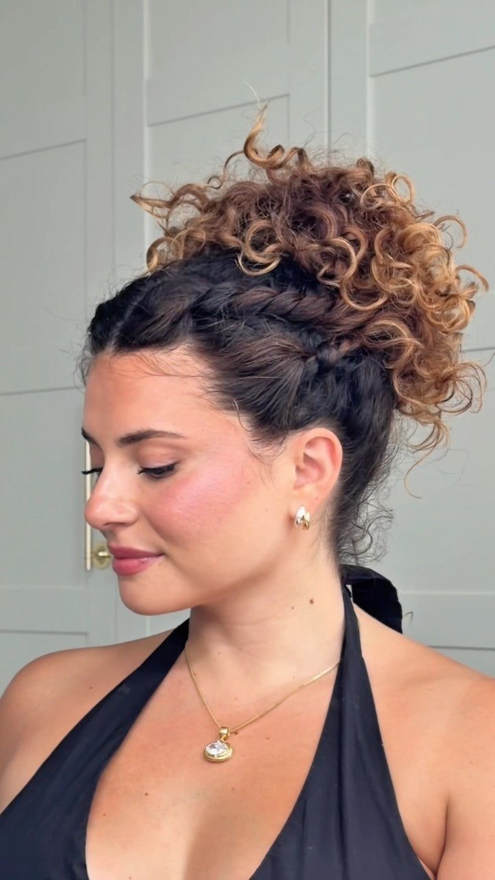 Woman with a braided crown and voluminous curly updo wearing a black top.