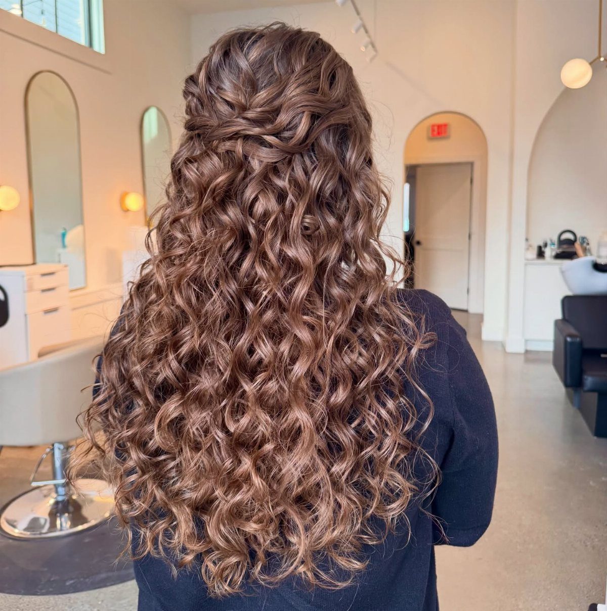 Long brown hair styled in defined ringlets with a half-up half-down design.