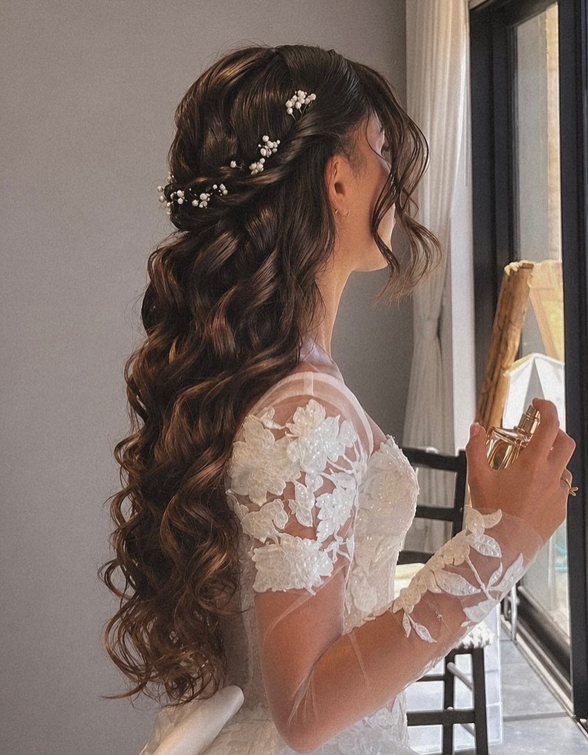 Woman with long brown cascading curls and small white floral hair accessories.