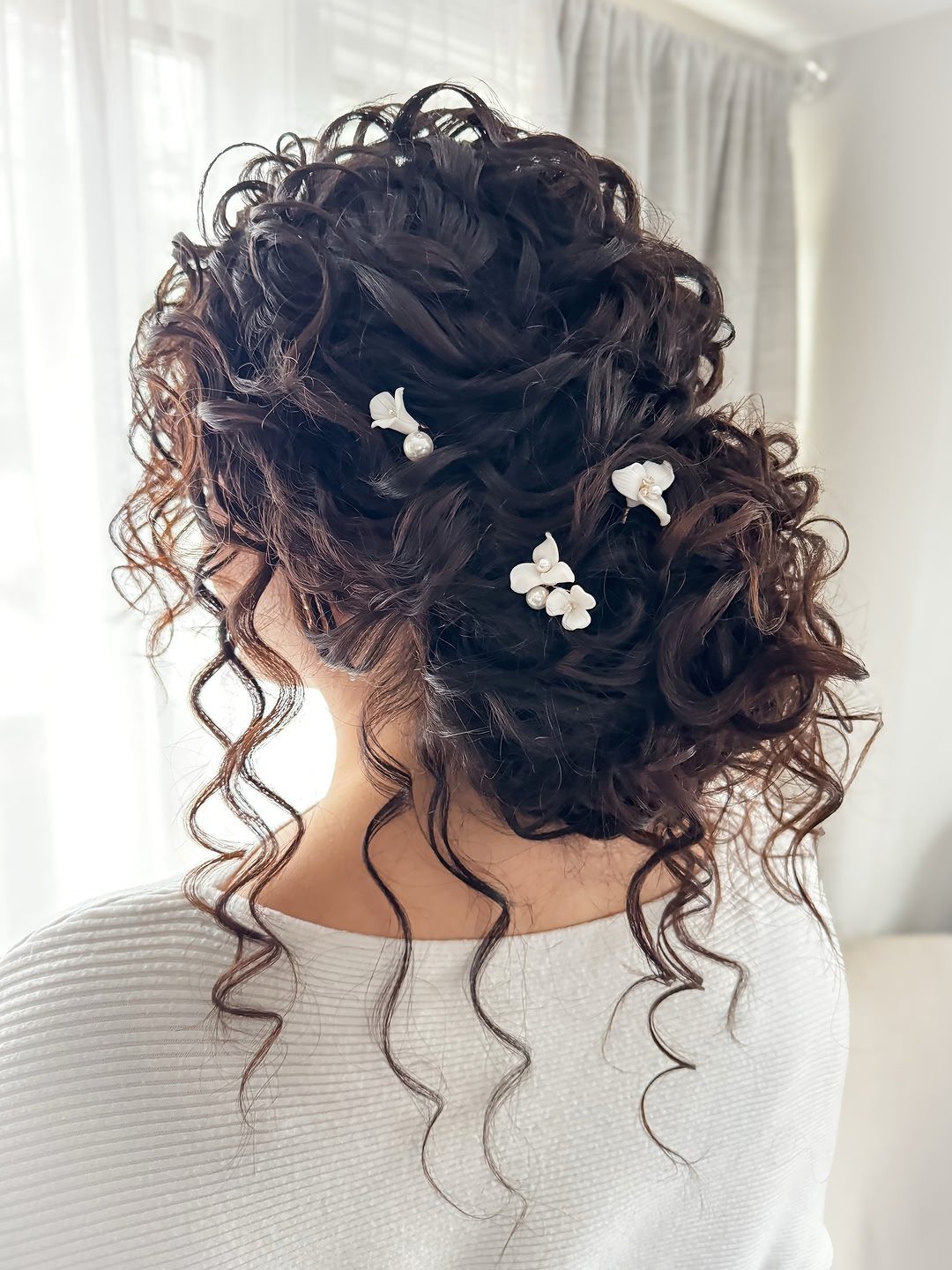 Dark brown curly hair updo with small white flowers tucked into the curls.