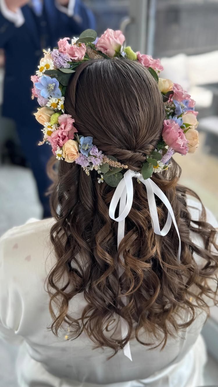 Brown curly hair adorned with a colorful floral crown and white ribbon.