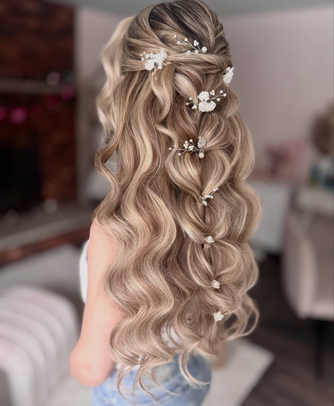 Long blonde curly hair with small white floral accessories pinned throughout the waves.