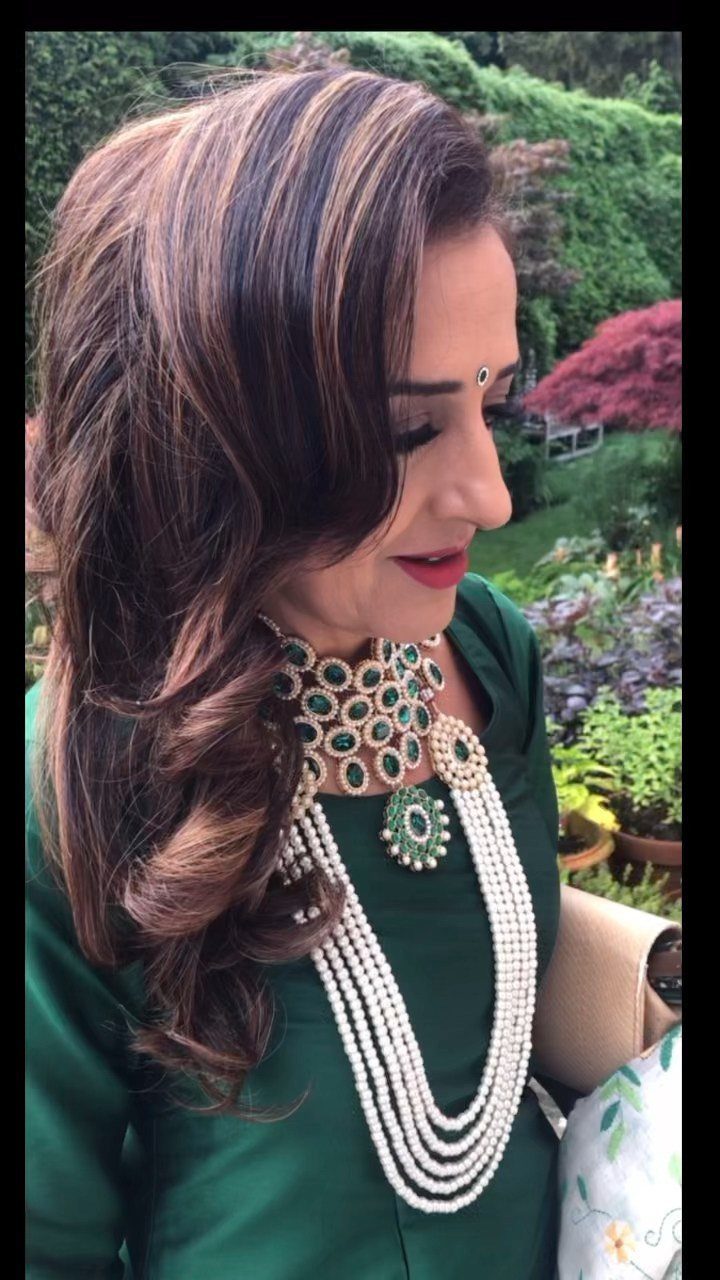 Woman with highlighted curly hair swept to one side wearing a pearl necklace.
