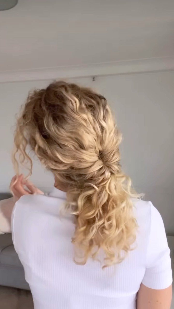Blonde curly hair styled in a low ponytail worn by a woman in a white shirt.