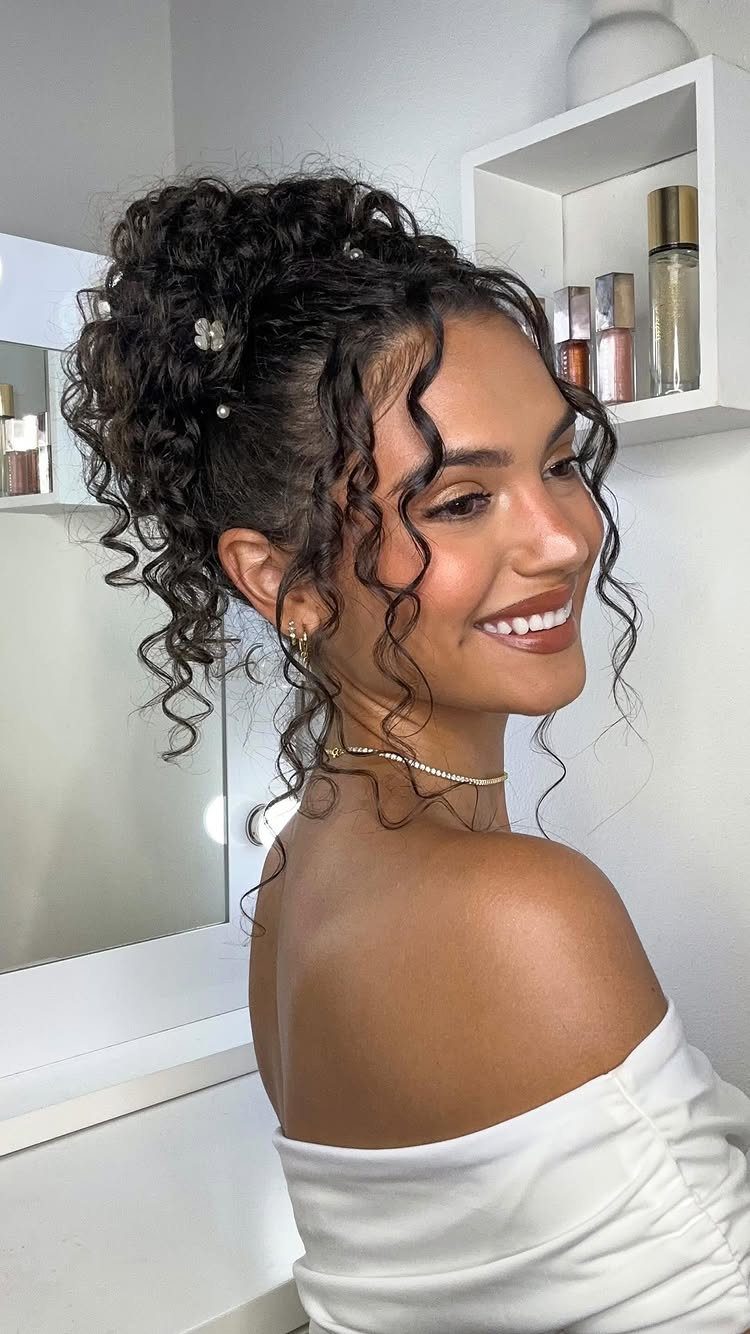 A smiling woman with dark curly hair styled in a high puff ponytail with face-framing curls.