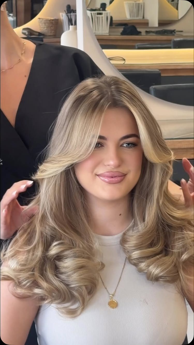 A woman with voluminous blonde hair styled in large, bouncy, glamorous blowout curls.