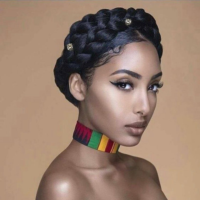 A woman with dark hair styled in a thick, braided halo crown and winged eyeliner.