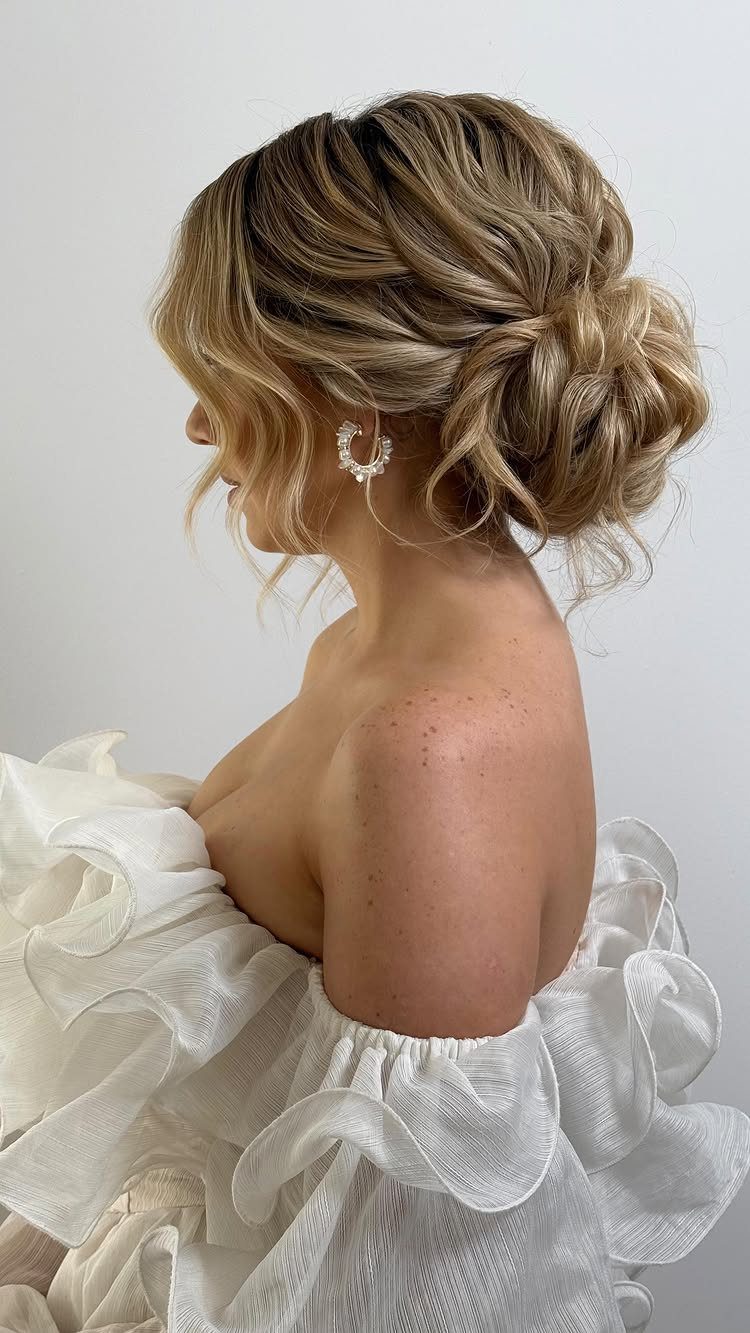 10 Easy Updos for Medium Hair for Wedding Guest Season 2026 4 A woman with blonde wavy hair styled in a textured low chignon bun.