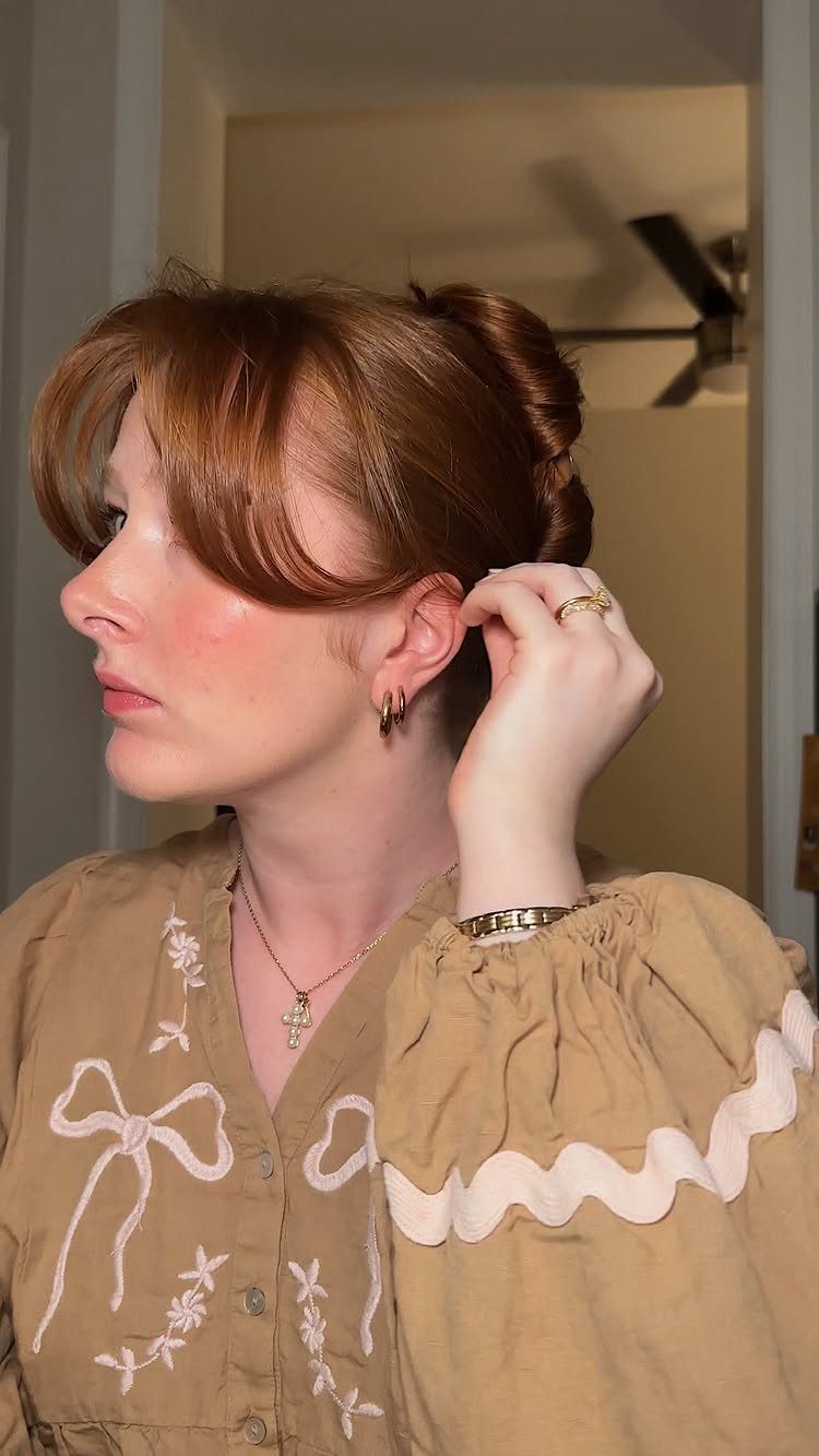10 Easy Updos for Medium Hair for Wedding Guest Season 2026 8 Woman with reddish hair styled in an elegant updo featuring soft, sweeping bangs.