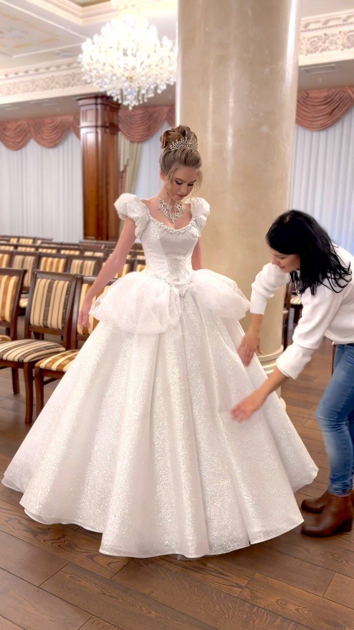 Elegant Princess Wedding Dress Styles in 27 Ideas 22 Woman in a sparkling white princess wedding dress being assisted in a grand hall.