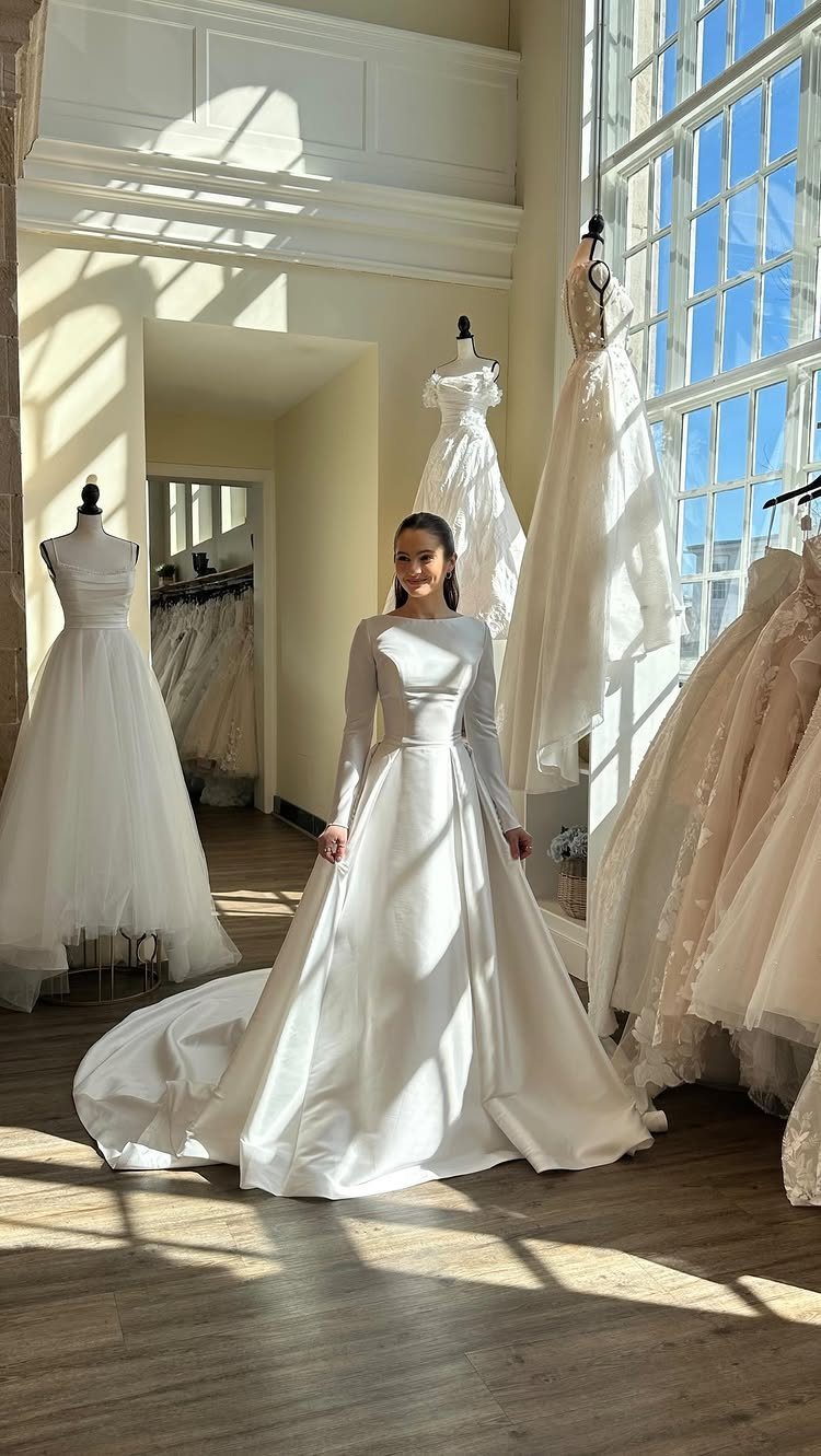 Elegant Princess Wedding Dress Styles in 27 Ideas 26 Woman in a white satin long-sleeved princess wedding dress in a bright bridal shop.