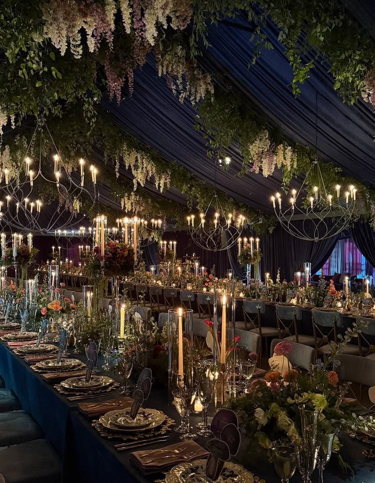 Enchanted Forest Theme Wedding: 12 Ideas for the Ceremony and Reception 9 Floral installations and candle chandeliers hang above a long, decorated banquet table in a dark room.