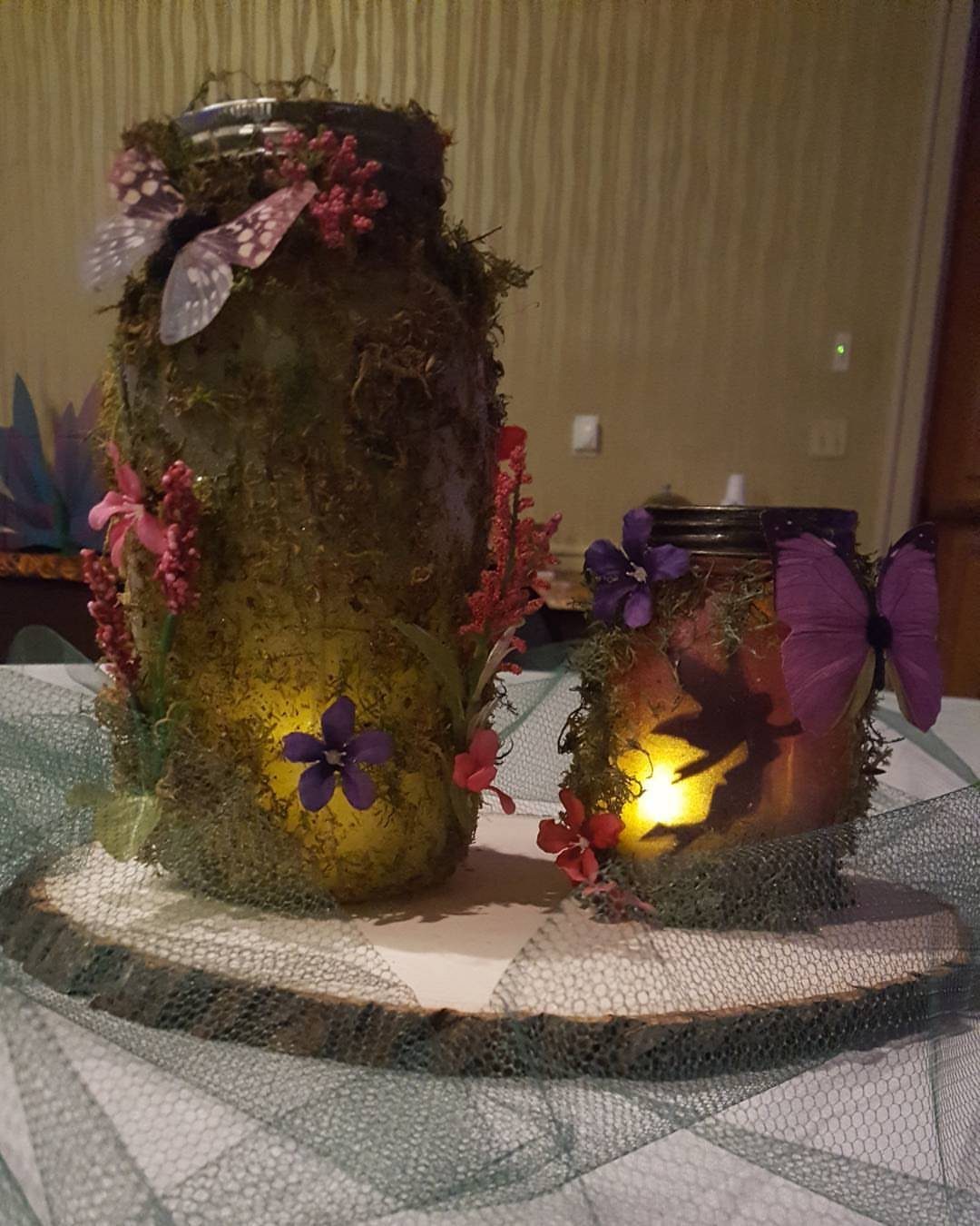 Enchanted Forest Theme Wedding: 12 Ideas for the Ceremony and Reception 2 Two glowing moss-covered jars decorated with colorful flowers and butterflies on a wood slice.