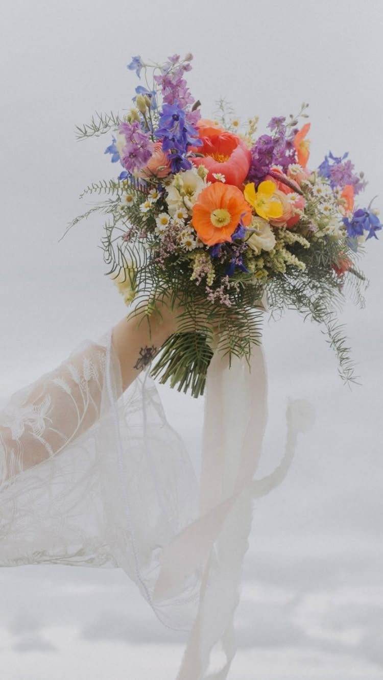 Enchanted Forest Theme Wedding: 12 Ideas for the Ceremony and Reception 8 A colorful wildflower bouquet with orange poppies and purple flowers held against a bright background.