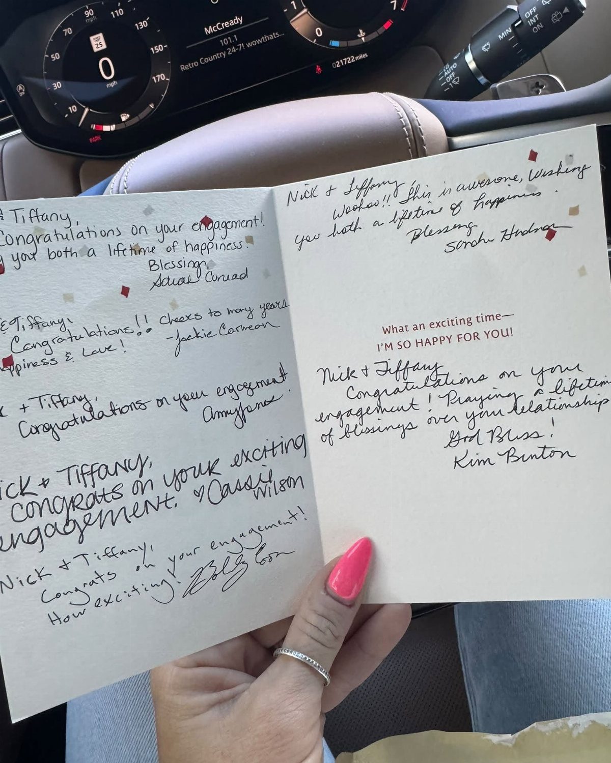 Handwritten engagement messages on a white card held by a person in a car.