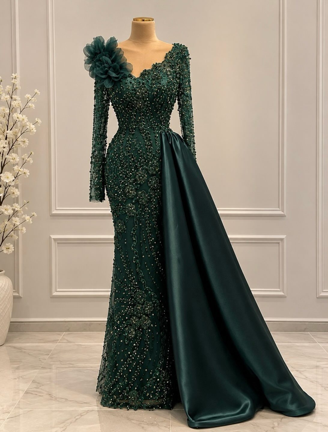 Emerald green beaded formal gown with a long satin train on a mannequin.