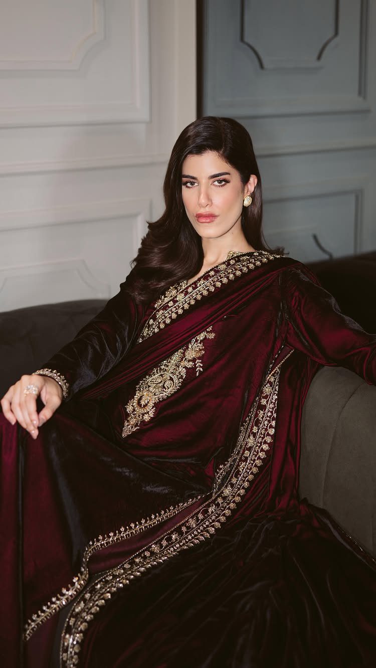 Woman in a rich burgundy velvet dress with gold embroidery sitting on a sofa.